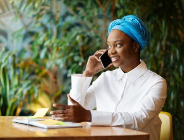 Cheerful pretty young black woman have phone conversation, cafe interior